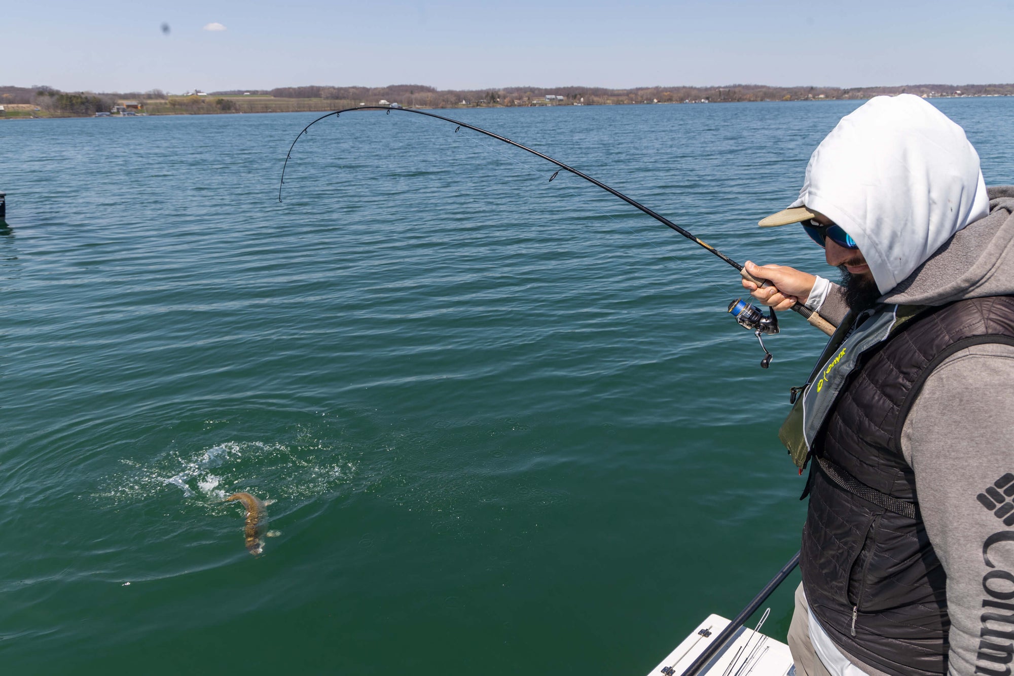 A man hooked a fish and is holding onto his pole, while the fish is thrashing around in the water.