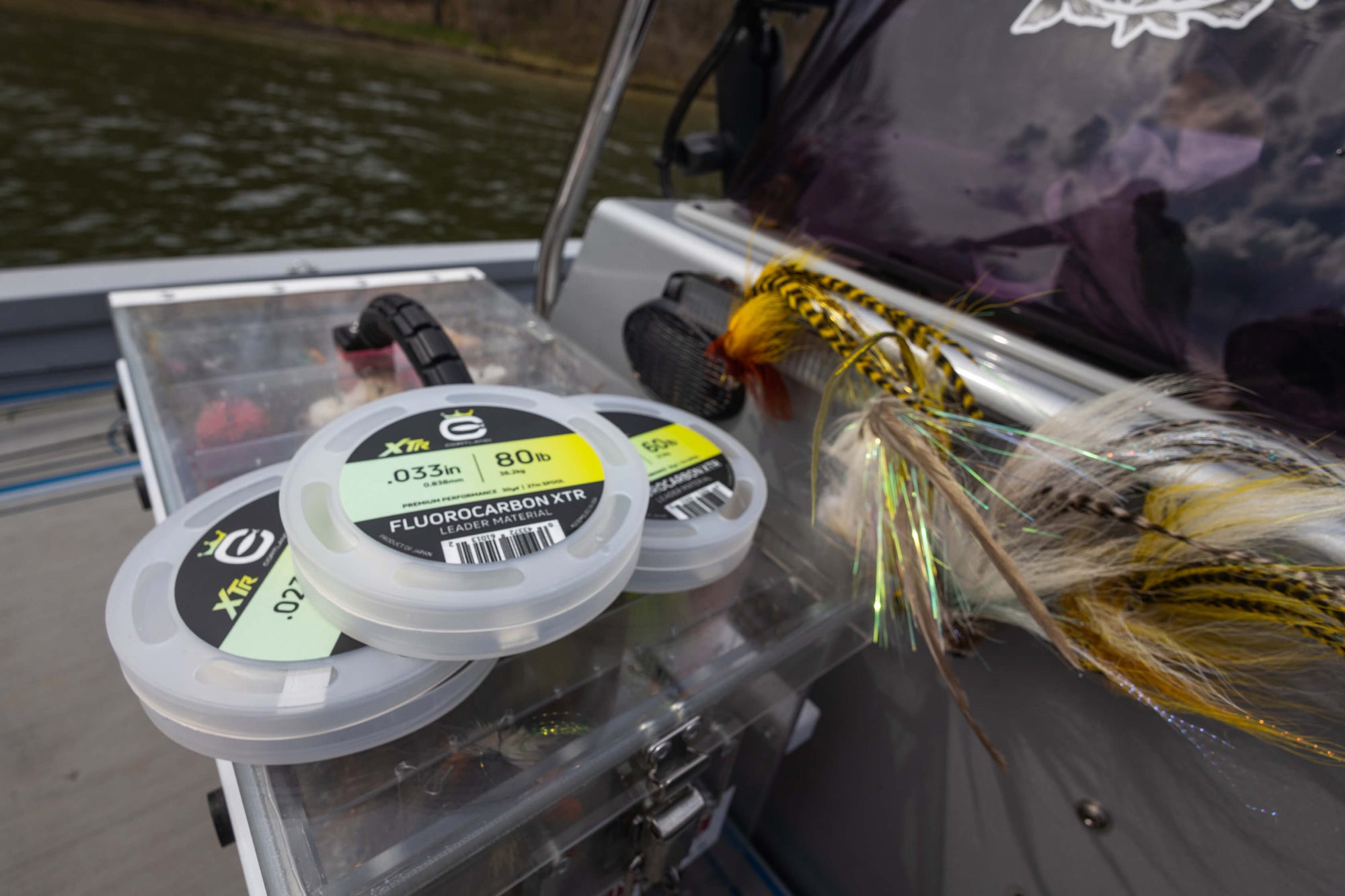 Flurocarbon XTR Leader Material. Three various spool sizes on a tackle box, with water in the background.