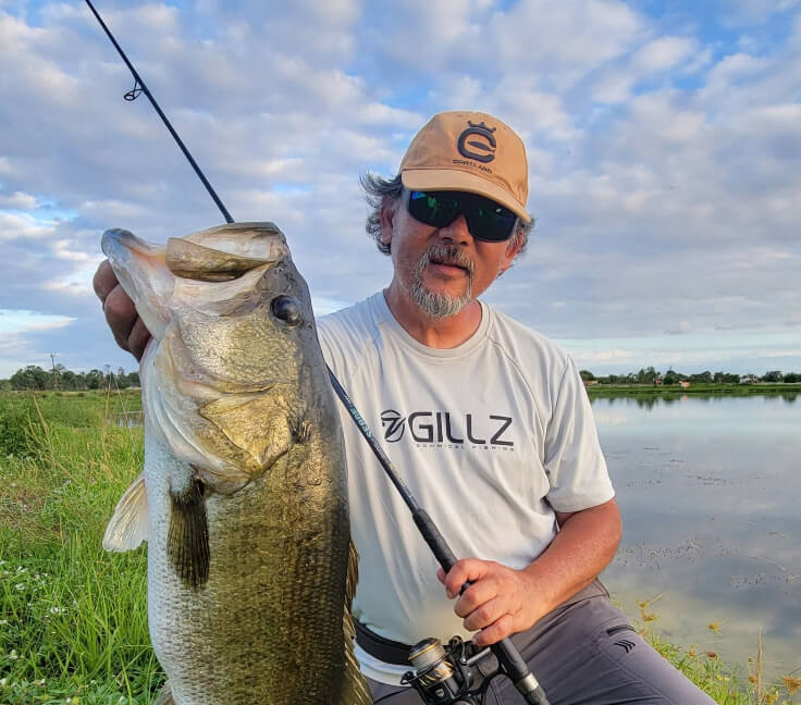 Alberto holding up a fish by its mouth and fishing pole in the other hand