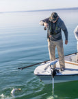 Two anglers are standing on a boat. One has prepared the net, while the other is reeling in the fish he caught.