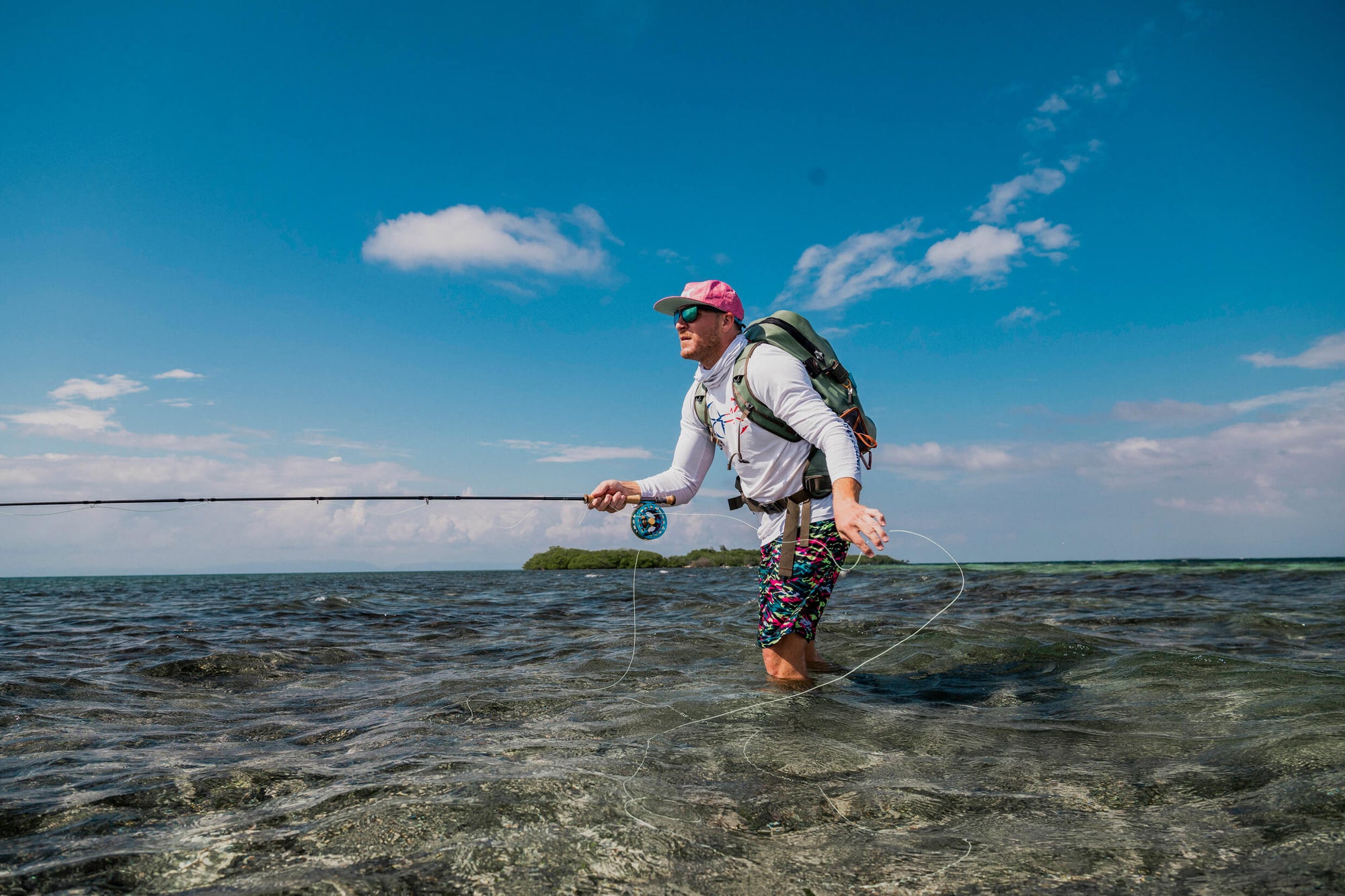 An angler fly fishing in clear knee high water with a bright blue sky. 