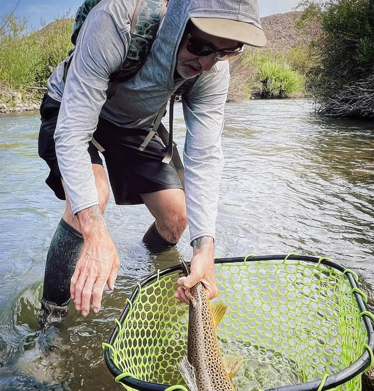 Matt Koles leaning over in a body of water, as he is holding onto a fish that is in a net