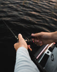 A pair of hands holding onto a fishing pole and their line is in the water.