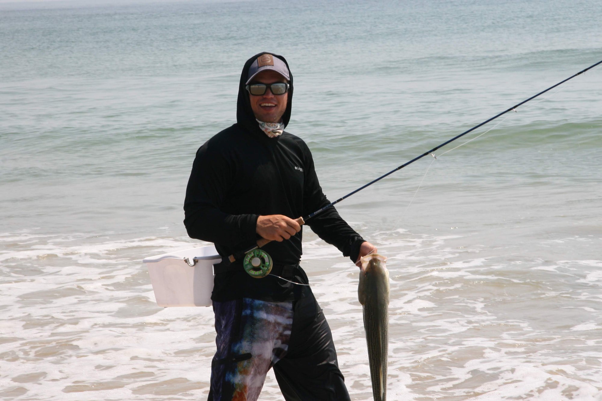 A fisherman smiling while holding up his fly rod and a fish