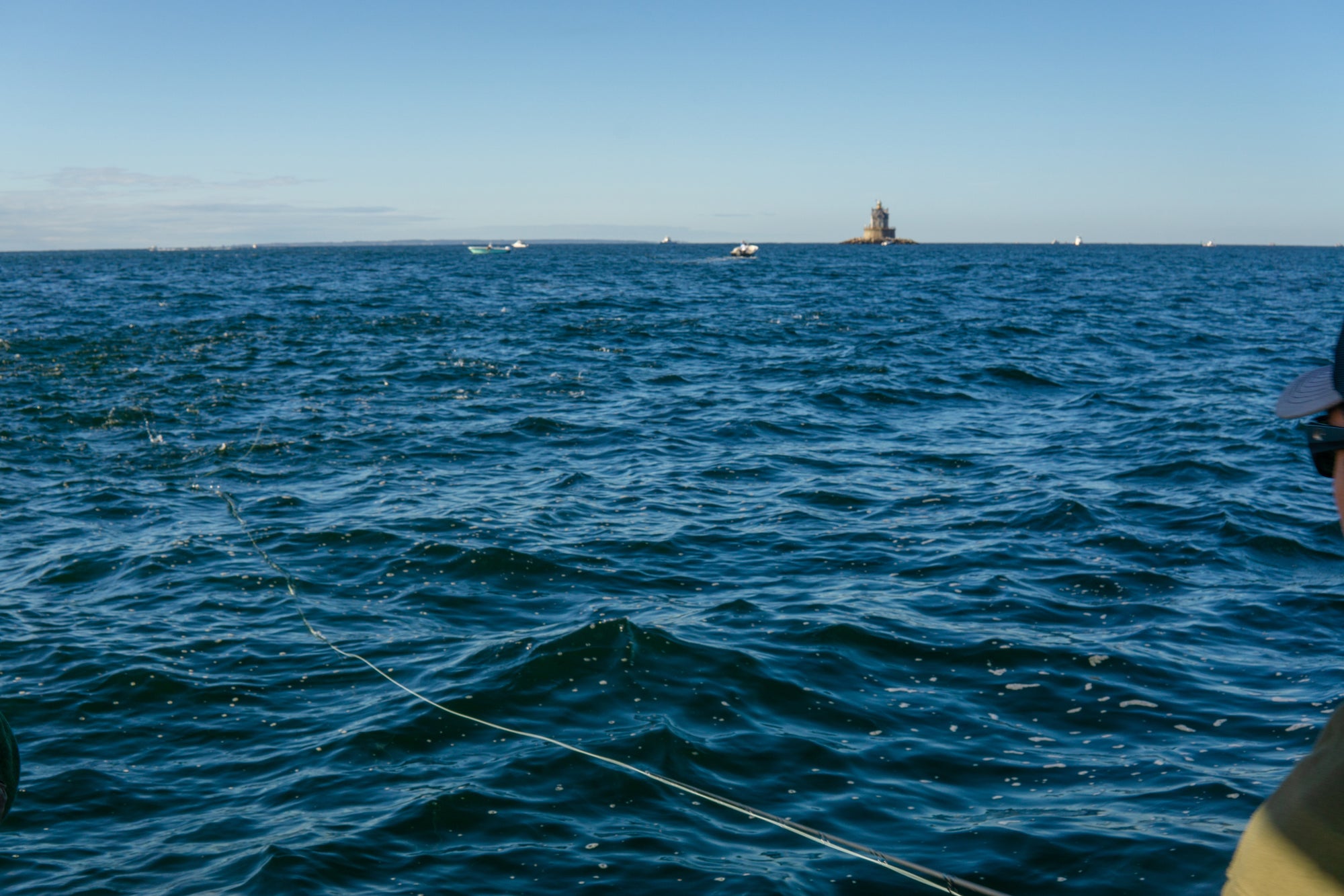 Someone is fishing on a large body of water, with his line cast and boats in the background.