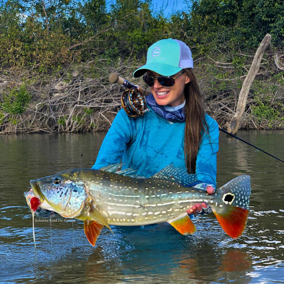 A girl is standing in waist high water and holding onto a fish.