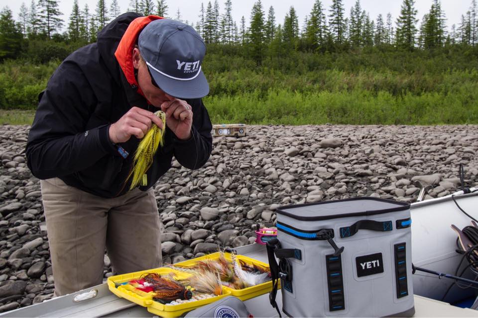 Fisherman is biting his fly line, while holding onto a fly fishing fly. 