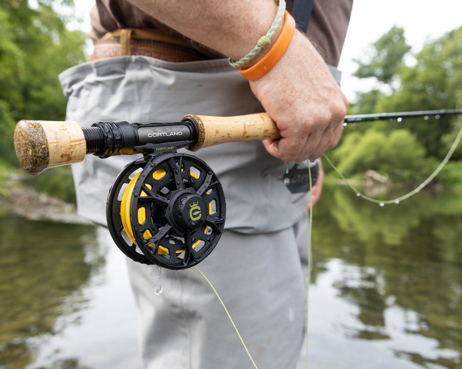 Hand on a fly rod and reel at the edge of a river