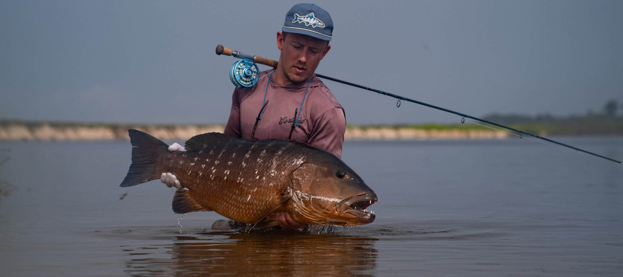 Angler standing in water, while holding onto a large brown fish