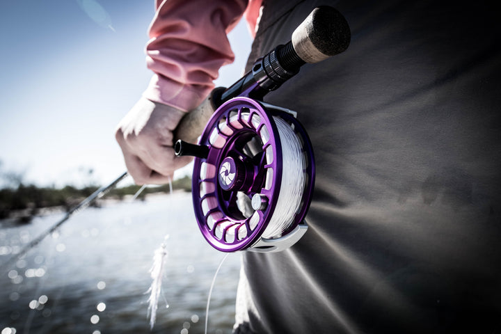 Closeup shot of someone holding onto a fly rod and the reel is purple 
