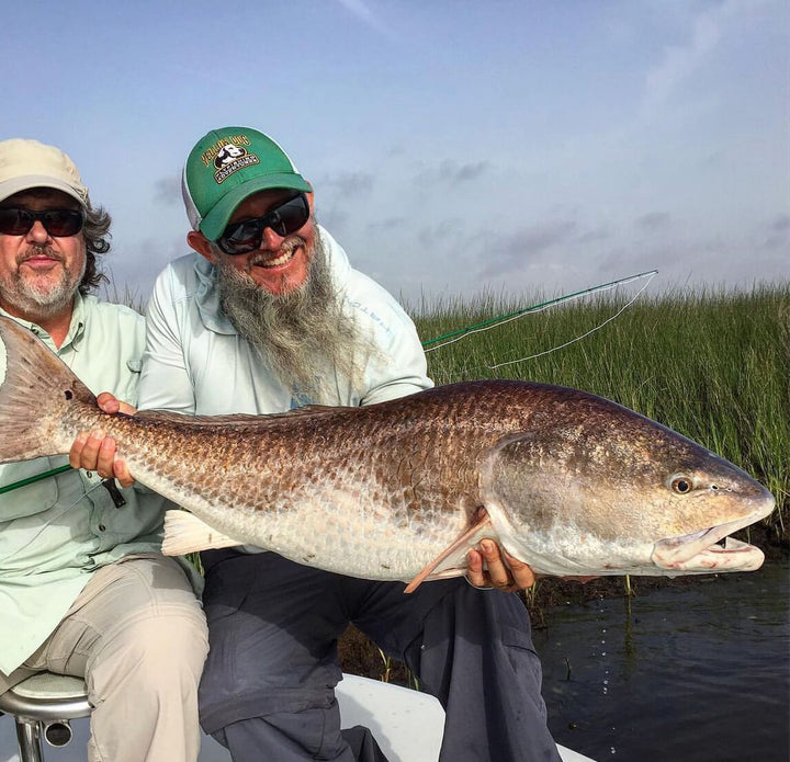 Greg Moon holding up a large fish across his lap with another fisherman seated next to him