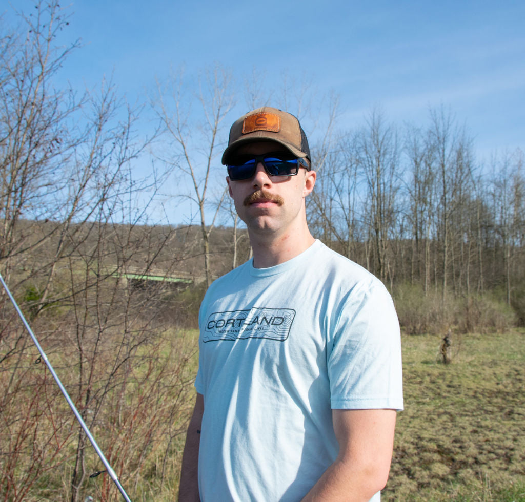 A man is looking directly at the camera with a fishing pole in one hand 