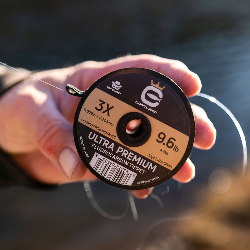 Cortland ultra premium fluorocarbon tippet spool held by a person with water in the background