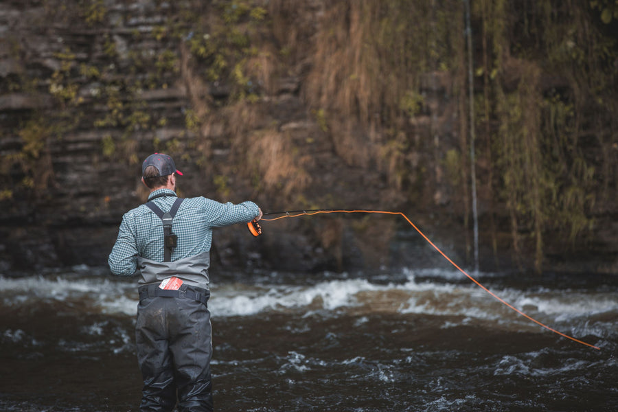 A man standing in a flowing river, while he is casting his fly line. 