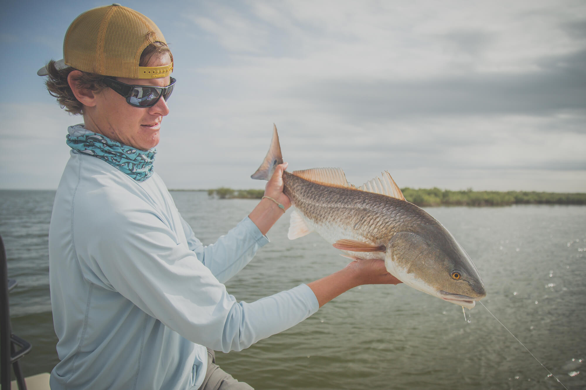 A man is holding up a redfish with water in the background. 