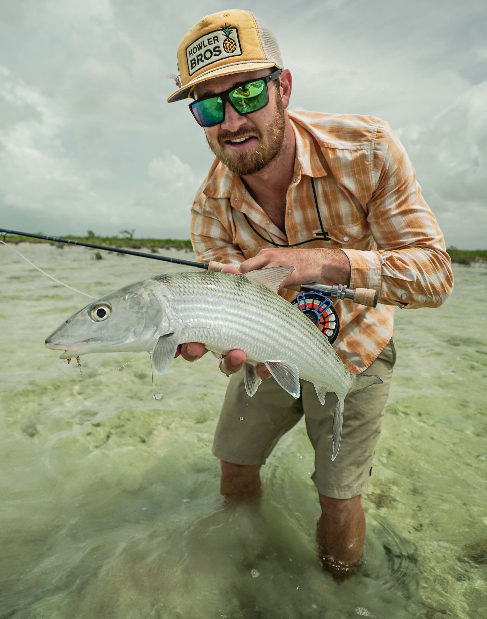 A man is standing in ankle high water and holding onto a bonefish. 