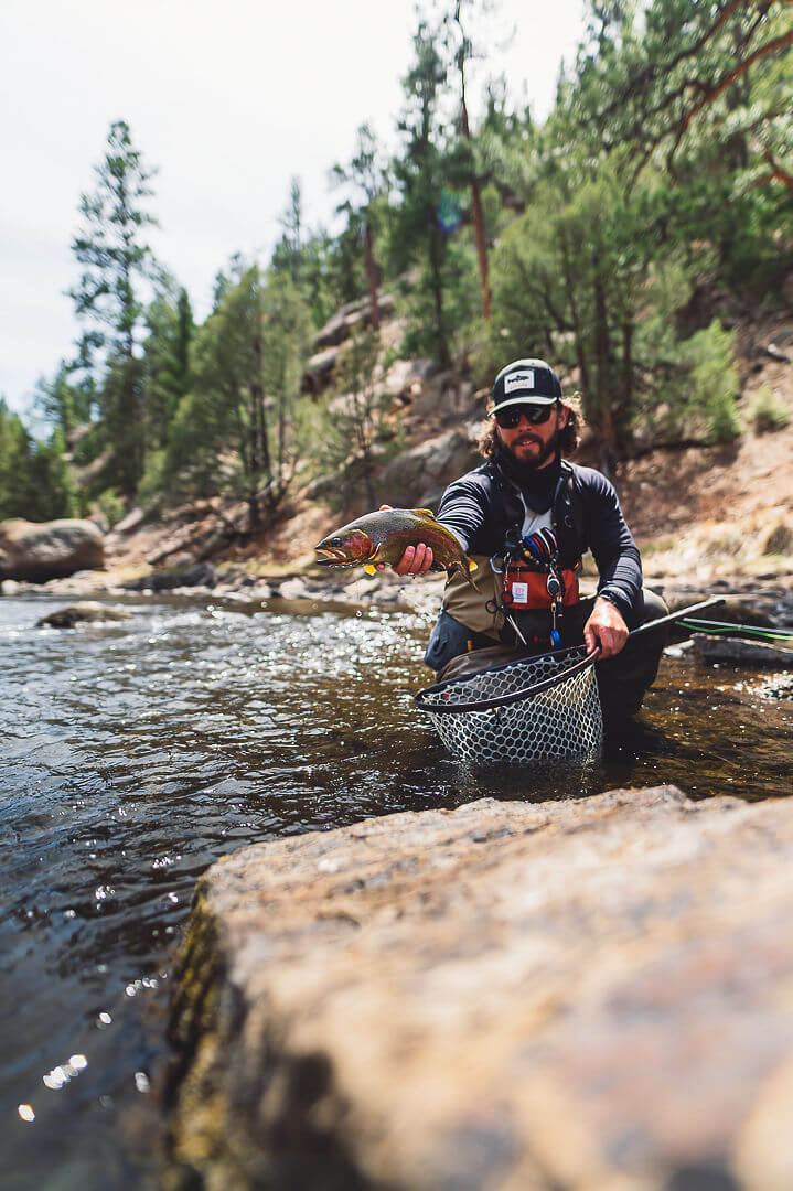 Fisherman kneeling in water, and holding onto a fish and fishing net