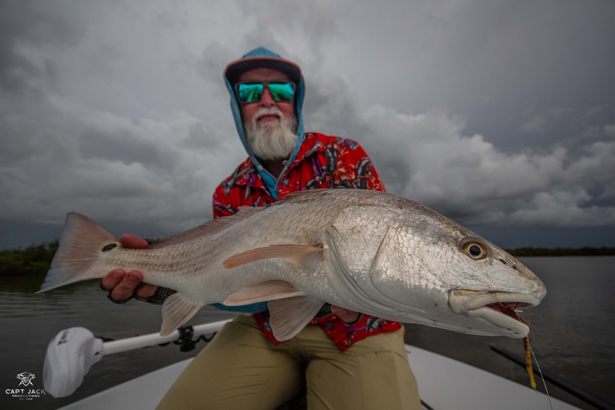A fisherman is seated on a boat and holding onto a redfish. 