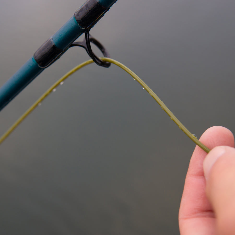 Closeup shot of a hand holding onto a fly line that is going through a fishing pole loop. 
