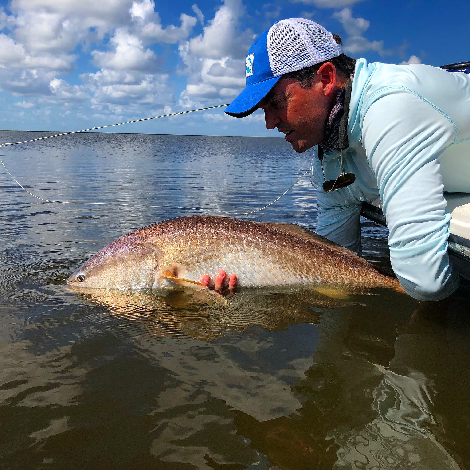 A man is leaning over a boat and holding onto a redfish in water. 