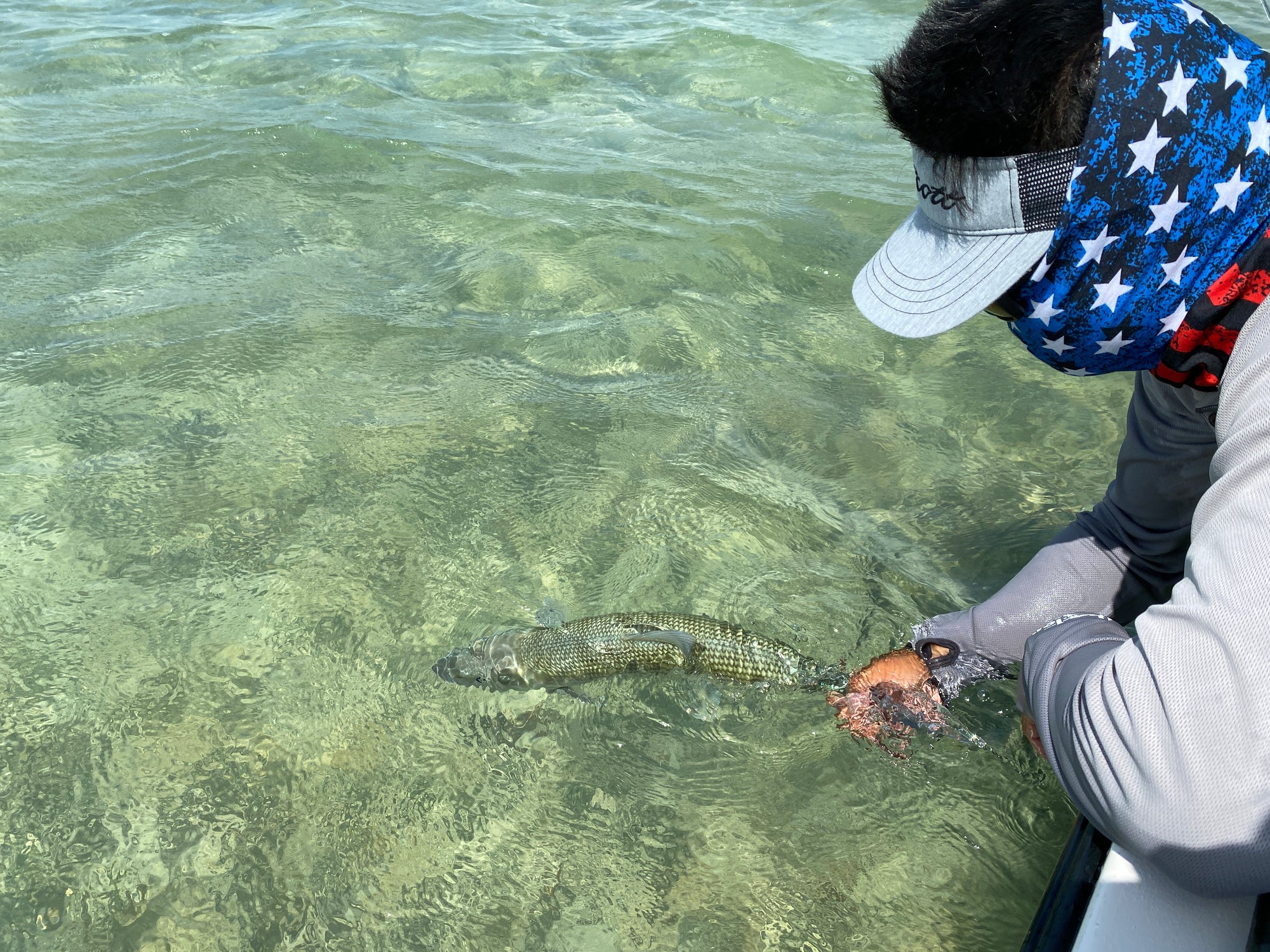 Someone leaning over a boat and holding onto a fish that is underwater. 